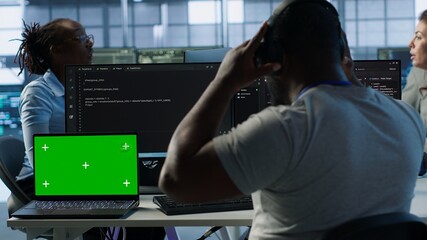 Isolated screen laptop next to programmer coding in server farm while listening music in...