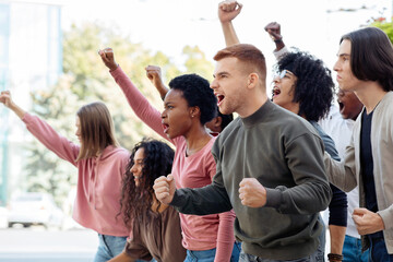 Side view of multiracial group of students chanting slogans and showing fists during demonstration,...