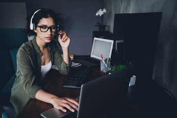 Young female professional working at a computer in a home office environment with headphones and...
