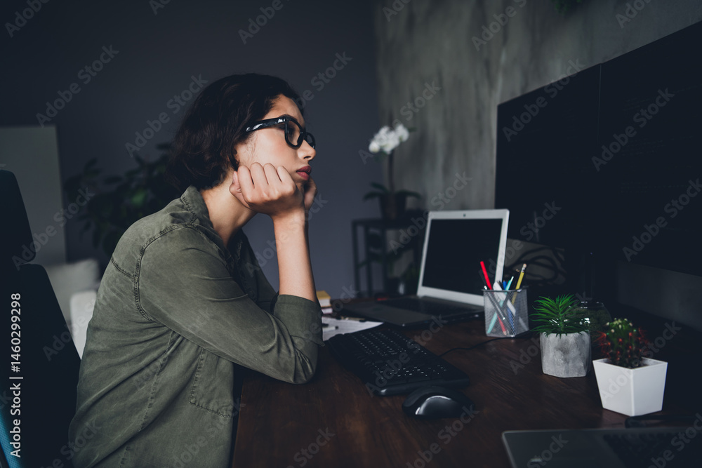 Poster young female programmer in a casual workspace focused on tasks with a computer and plants on a woode