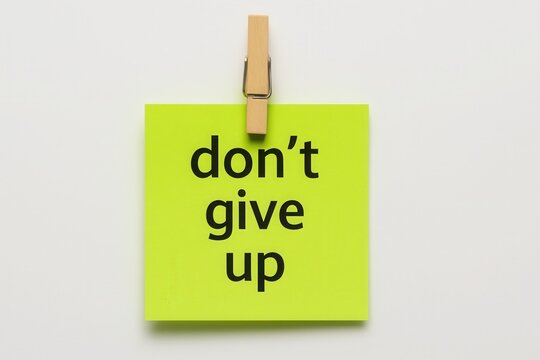 A bright yellow sticky note with a strong message, "Don't give up," emphasizing perseverance and motivation to keep going