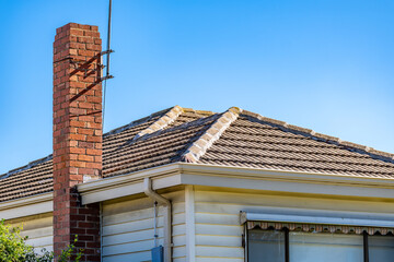 A mid-century suburban Australian house featuring a red brick chimney, tiled roof, and weatherboard...