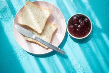 Spreading strawberry jam on toast bread on pink plate in close-up
