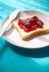 Spreading strawberry jam on toast bread on pink plate in close-up