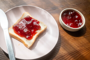 Spreading strawberry jam on toast bread on pink plate in close-up