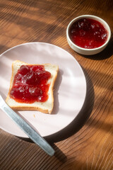 Spreading strawberry jam on toast bread on pink plate in close-up