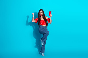 Excited Young Woman With a Red Phone Celebrating Success on a Vibrant Blue Background