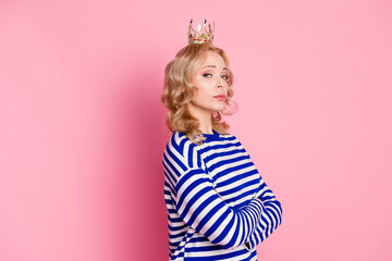 Portrait of a young stylish woman wearing a striped pullover and a crown, posing confidently against a pink background
