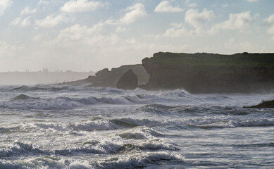 view of an ocean coast with strong waves splashing against the tall rocks under the sunlight in the...