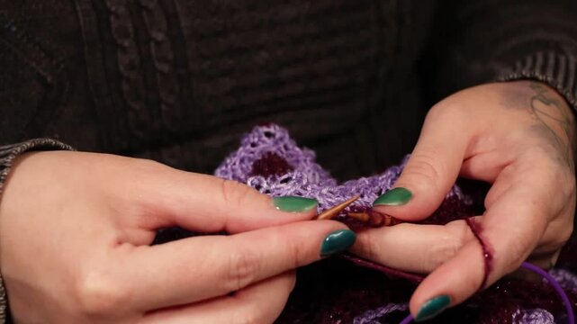 manos de mujer con u&ntilde;as pintadas tejiendo con lana violeta y agujas