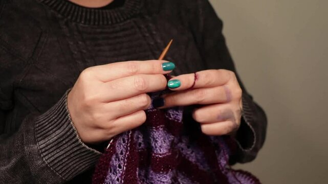 manos de mujer con manicura tejiendo con lana violeta y agujas