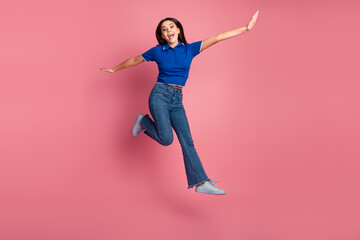 Happy young woman jumping joyfully in casual clothing against a pink background, expressing...