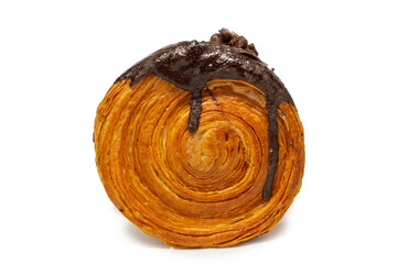 A close-up of a New York roll or Cromboloni, a round pastry with flaky layers and a chocolate glaze on top, isolated on a white background. 