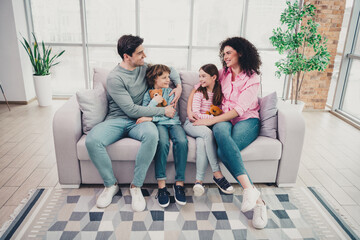 Happy young family bonding together on a cozy couch in their bright modern living room during a...