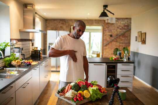 Middle aged male african american food nutritionist and blogger recording a video about a healthy recipe with organic fruits and vegetables in his kitchen at home