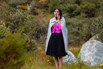 Campesina quechua en un campo con un celular, feliz mientras usa su smartphone, mirando un espacio publicitario y aislado en un entorno natural, contactando con su celular. Quechua. Montaña. 