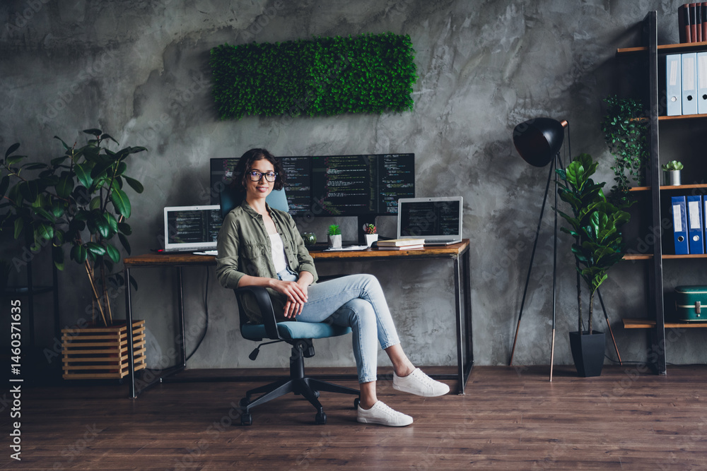 Aufkleber young female programmer in casual attire sitting at a stylish home office with multiple screens disp