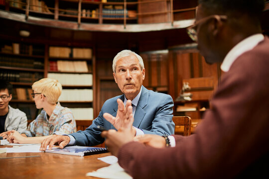 Young and diverse group of students studying in a university library with the help of their professor