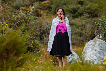 Campesina quechua en un campo con un celular, feliz mientras usa su smartphone, mirando un espacio publicitario y aislado en un entorno natural, contactando con su celular. Quechua. Montaña. 