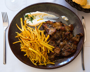 Plate of grilled lamb meat served with fried potato straws and sauce