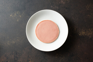 A top down view of a slice of bologna on a plate. © DAVID