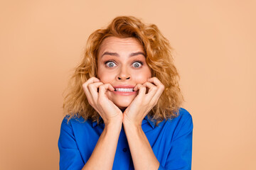 Young red haired woman biting her nails, expressing surprise and worry, wearing a blue shirt...