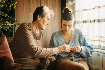 Senior caucasian woman teach granddaughter how to knit with needles