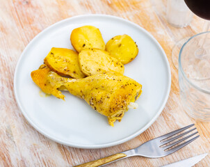 Delicious chicken thighs served with baked potato slices on plate