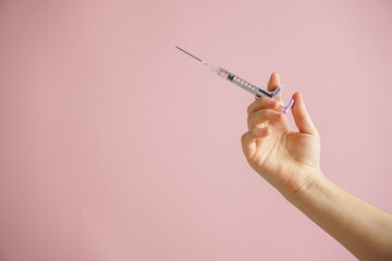 gloved hand holding multiple colorful syringes, against a soft background. Conceptual image related...