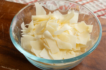 A view of a small glass bowl of shaved parmesan cheese.