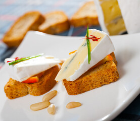 Delicious canapes on toasted bread with soft blue cheese and orange slice served on white plate