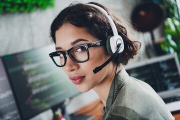 Young female programmer working on a computer with coding on screen wearing a headset in casual workspace