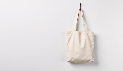 Minimalist beige canvas totebag mockup hanging on white wall with soft studio lighting
