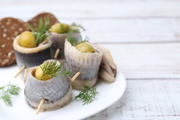 Delicious herring rolls with olives, dill and bread on white wooden table, closeup. Space for text