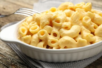 Delicious pasta with cheese sauce and fork on wooden table, closeup