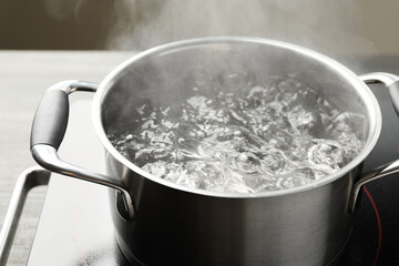 Cooking pot with boiling water and stove on table against grey background, closeup
