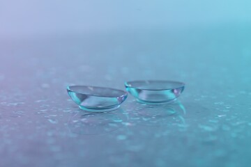 Pair of contact lenses and water drops on color gradient mirror surface, closeup