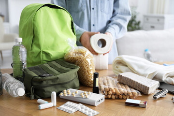 Survival kit. Woman packing different emergency supplies at wooden table indoors, closeup