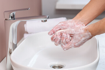 Woman washing her hands with soap above sink in bathroom, closeup