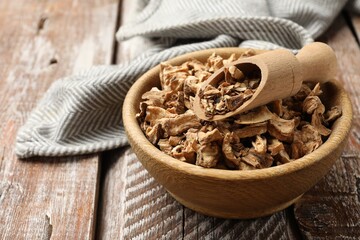 Pieces of dry chicory roots in bowl and scoop on wooden table, closeup