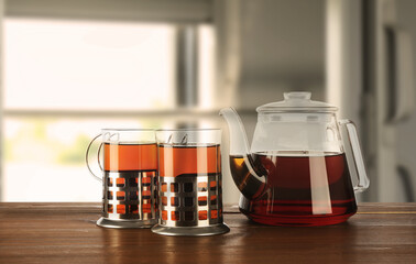 Glasses of freshly brewed tea in holders and teapot on table in train