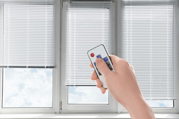Woman using remote to control blinds in room, closeup