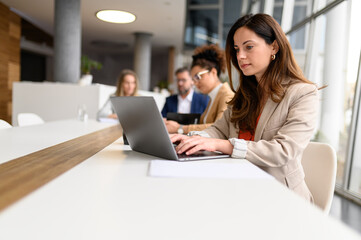 Focused female lawyer working online on laptop in boardroom while colleagues collaborate in the...