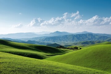Fototapeta premium Rolling green hills under a bright blue sky with distant mountains and scattered white clouds above them