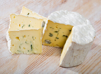 Wheel of delicate blue cheese with cut slices on wooden cutting board..