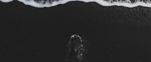 Foot in dark sand as ocean water washes shore in monochrome beach scene, nature?s power on display