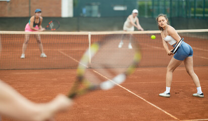 Two women tennis doubles players play against women on tennis court