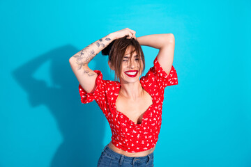 Young woman in red floral top smiling joyfully against vibrant blue background, expressing...