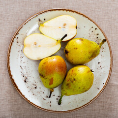Plate of pears is on table in center of picture. Juicy and ripe fruits shine appetitively in rays of sun. Concept of healthy diet and lifestyle
