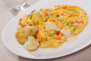Tasty omelet with vegetables served with baked cauliflower and delicate cheese sauce..